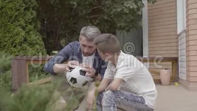 父亲和儿子坐在门廊上的肖像，手里拿着一个泄气的足球特写。 <strong>家庭开支</strong>